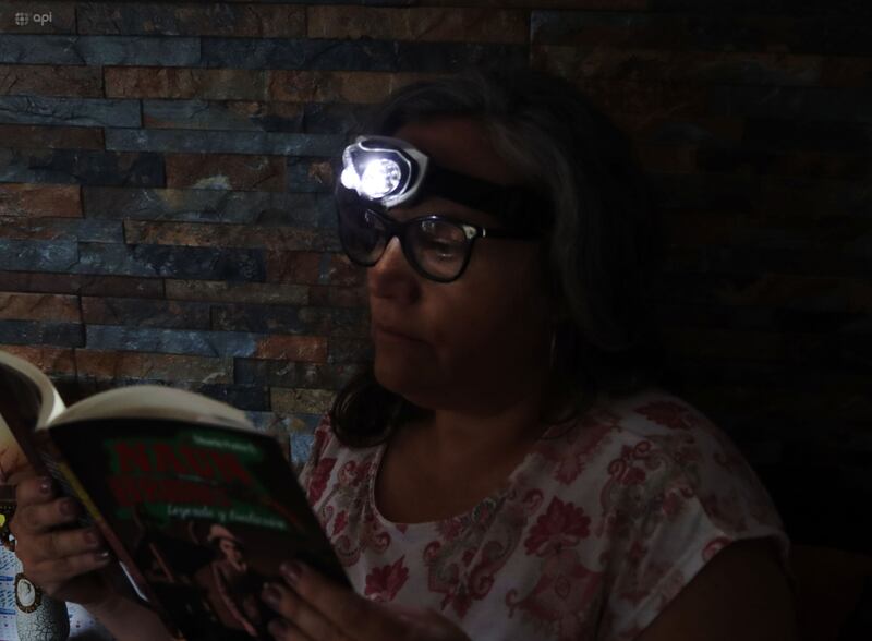 Una mujer leyendo un libro con una linterna en la cabeza en medio de los cortes de energía en Quito